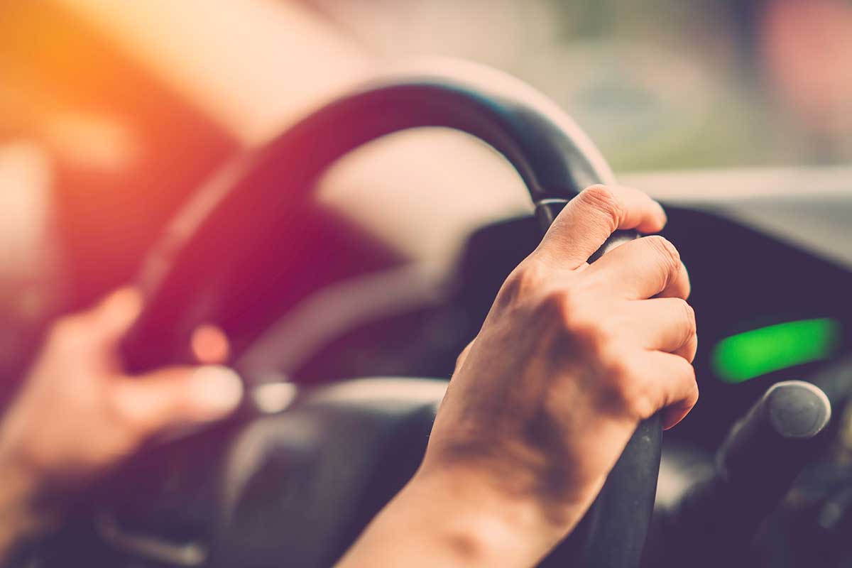 Hands holding driving wheel in the sunset